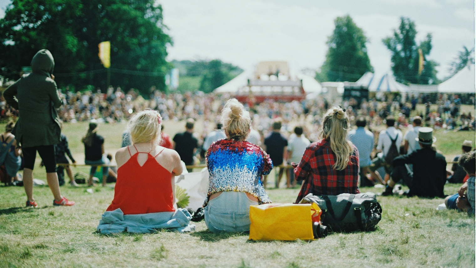 Three people sat on the grass at a festival
