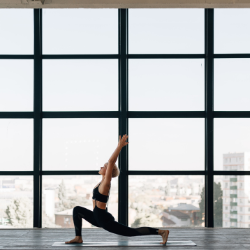 A woman doing a yoga lunge in front of a large window.
