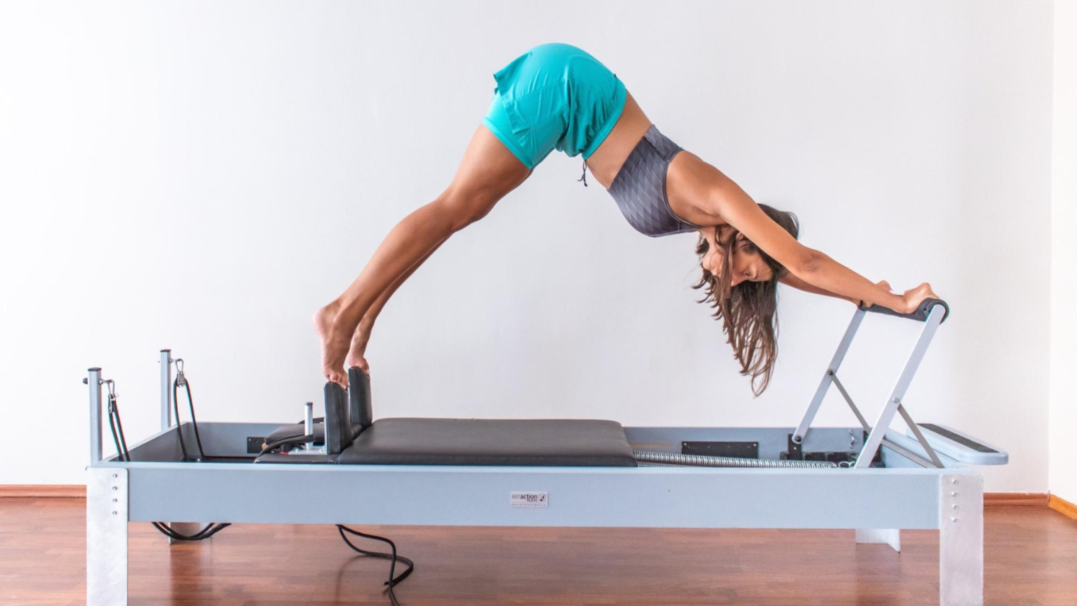 A woman on a reformer pilates machine in downward facing dog