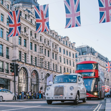 An image of Oxford Circus. A bus and a few cars are on the road, and there are multiple Union Jack flags hanging up. 