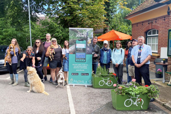 Group of walkers and dogs standing around a pull-up banner outside a railway station