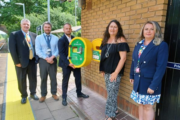 Group of 5 people standing with a defibrillator on the platform of Hedge End station in Hampshire