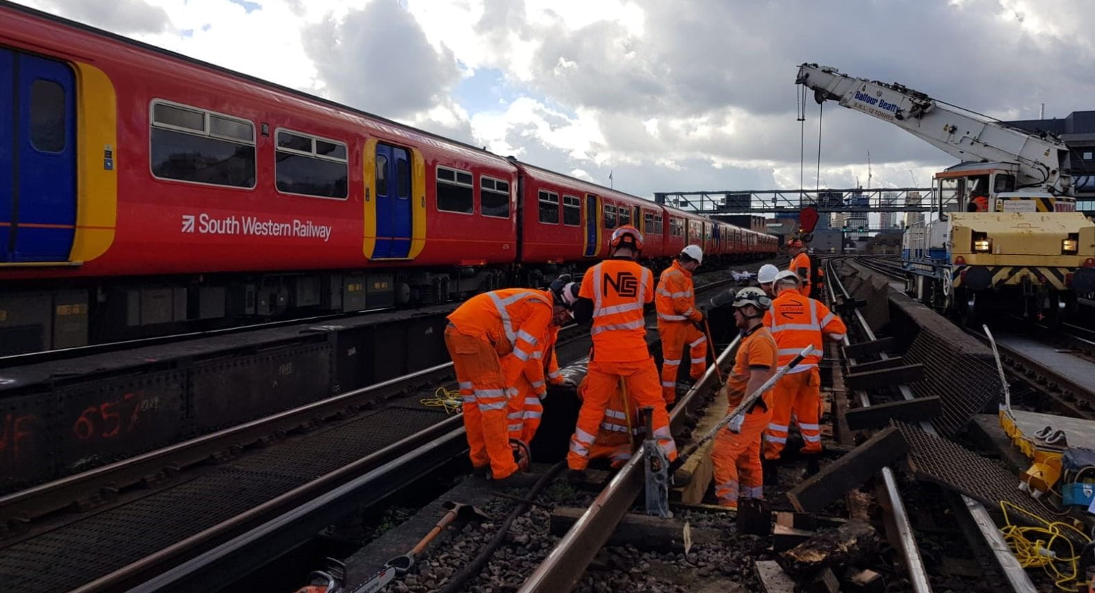Group of engineers wearing hi-visibility outfits working on the rail tracks beside a red SWR Class 455 train.