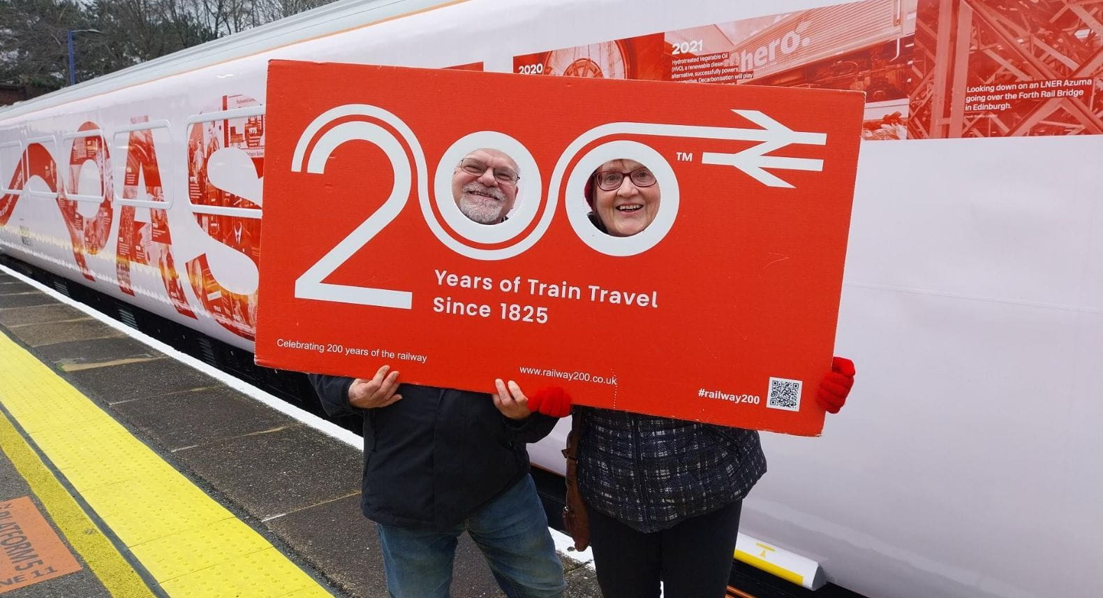 Two people looking through a cutout of the words Railway 200 beside the Inspiration train
