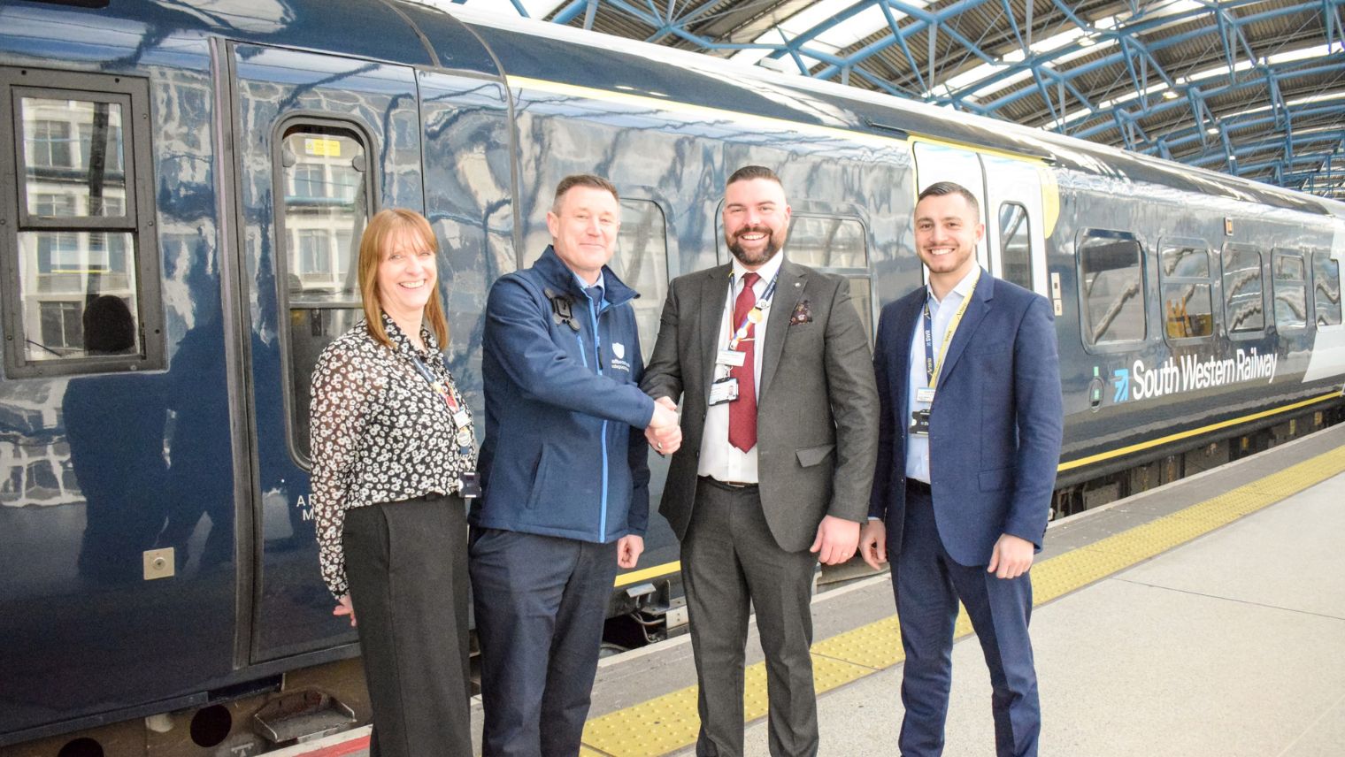 Group of four people standing beside a train - two in the middle are shaking hands