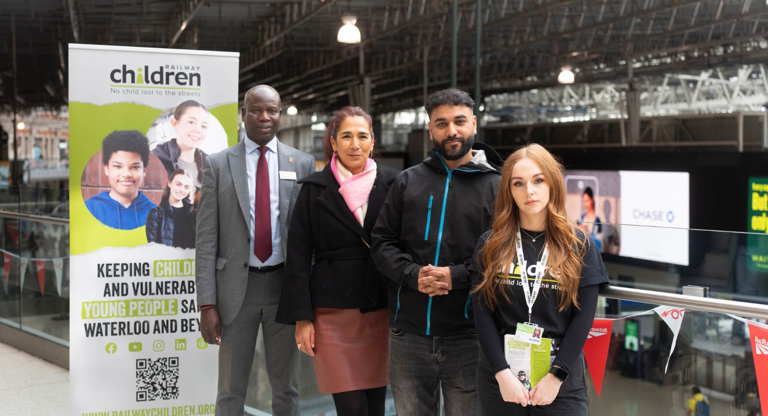 Group of four people standing in front of a Railway Children charity banner on the balcony of Waterloo station