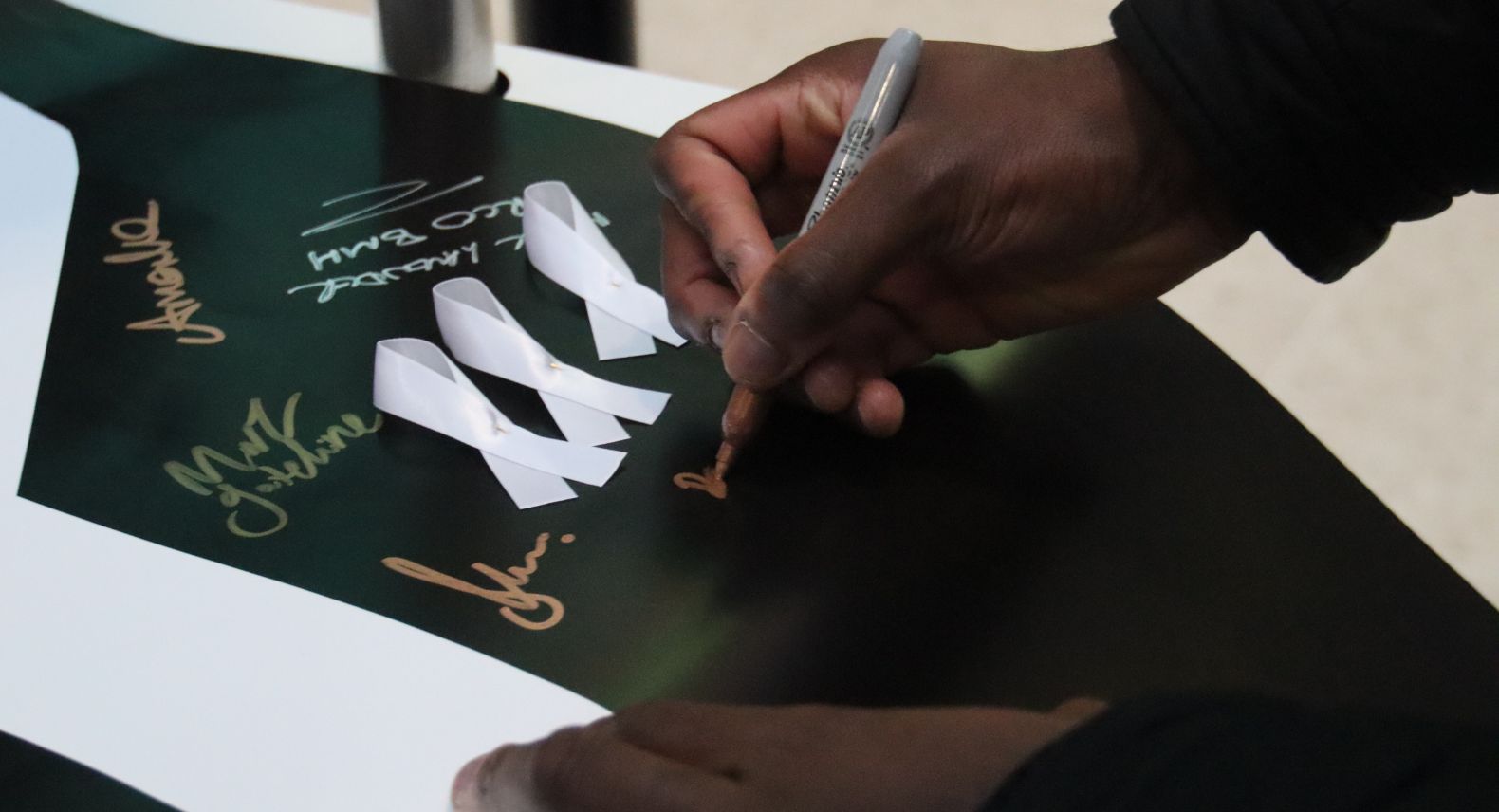 A hand signing the White Ribbon Day promise