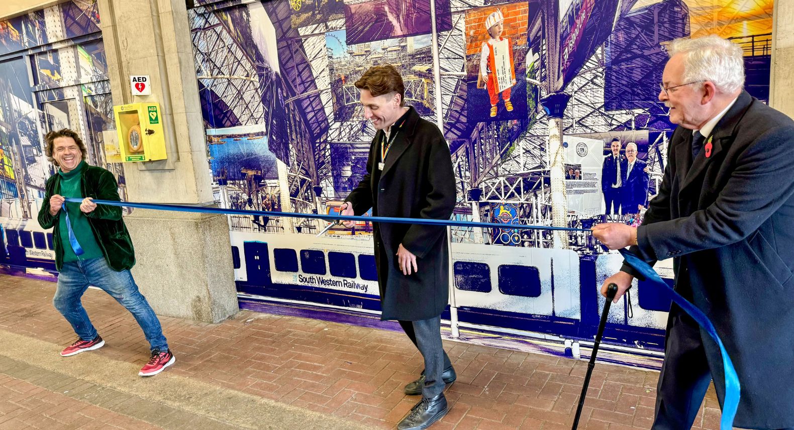 Ribbon cutting in front of a mural painted on a wall at Waterloo station