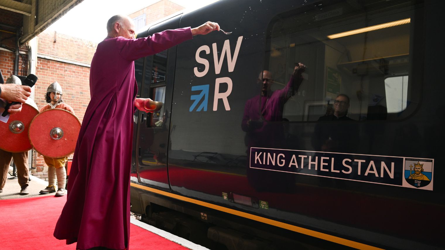 Bishop wearing a purple cassock sprinkles holy water on a train to bless it