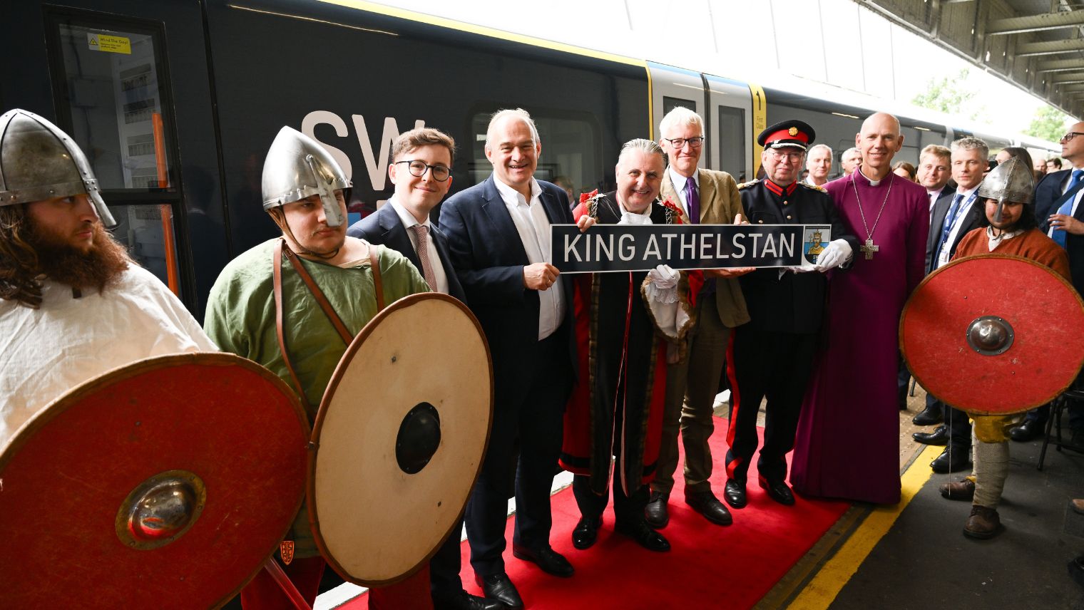 Group of people including a bishop and a Mayor in robes and a group of Saxon reenactors posing in front of a train