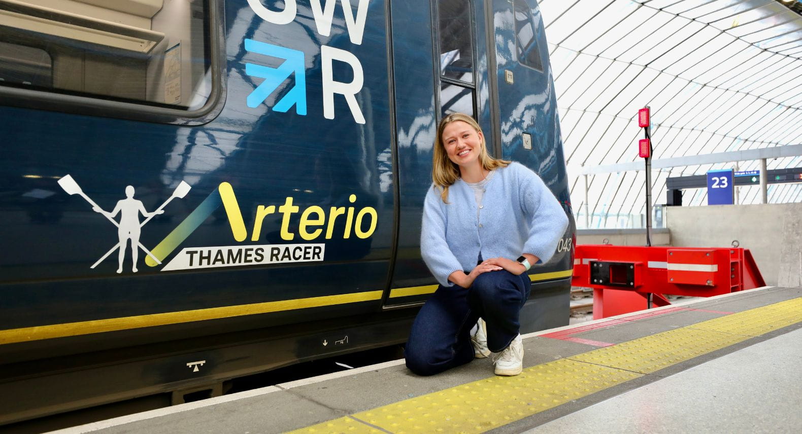 Blonde woman crouching beside a train that says Thames Racer