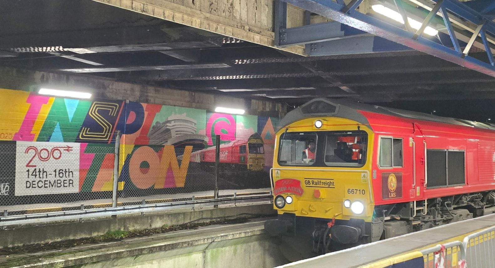 A red locomotive in front of a wall with a mural saying Inspiration and 200 14-16 December