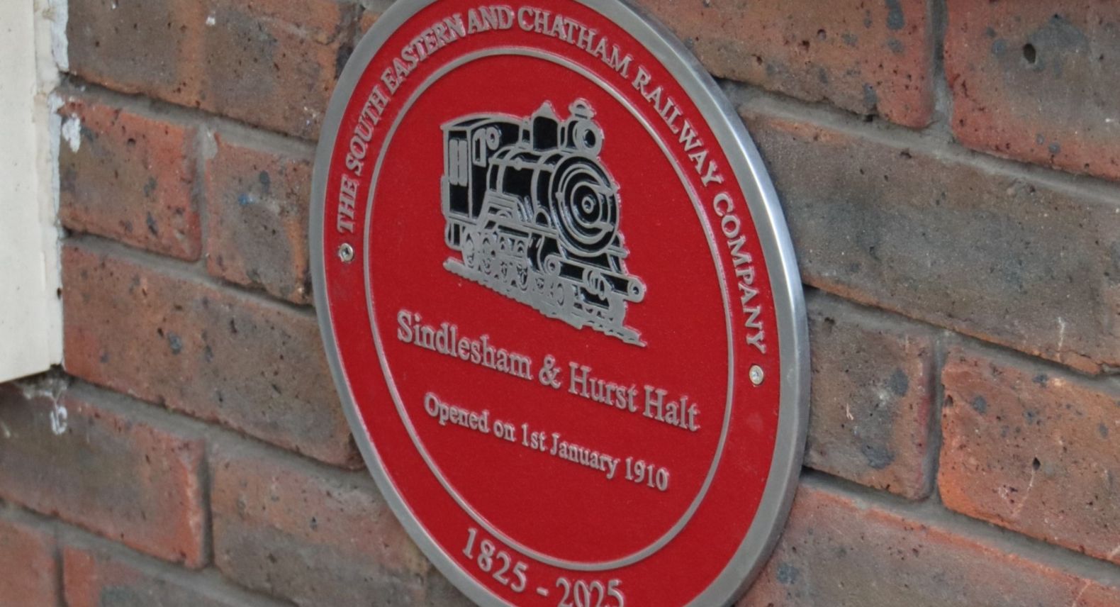 Round red plaque commemorating the opening of Sindlesham and Hurst Halt station in 1910
