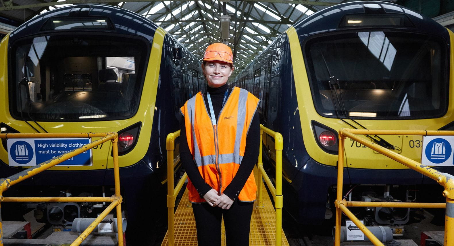 Person wearing a hi-vis tabard and cap standing between two Arterio trains