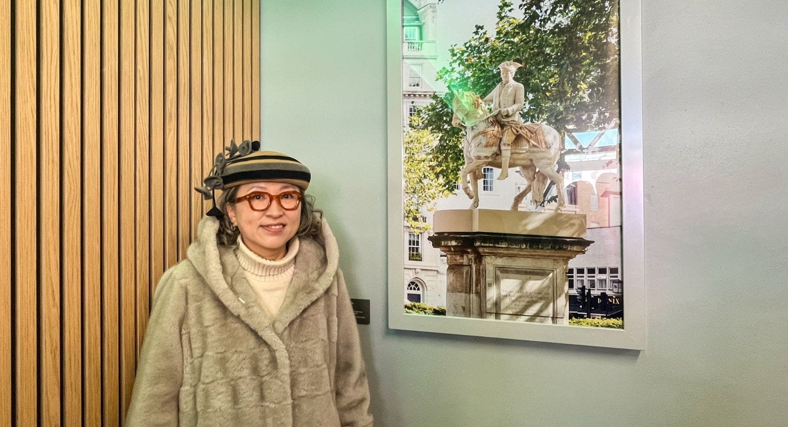 Korean artist Meekyoung Shin standing in front of a large photo of one of her artworks - a statue of a man on a horse