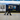 A woman dressed in dark clothing walks along a train platform, pulling a silver suitcase past a stationary South Western Railway Arterio train with “SWR” branding and blue and yellow detailing.