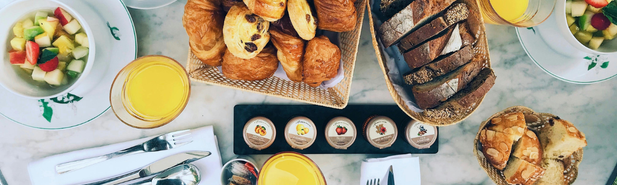 Pastries, fruit salad, jams, and orange juice arranged on a marble breakfast table