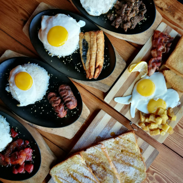 Breakfast plates with rice, sunny‑side‑up eggs, and assorted meats arranged on a wooden table.
