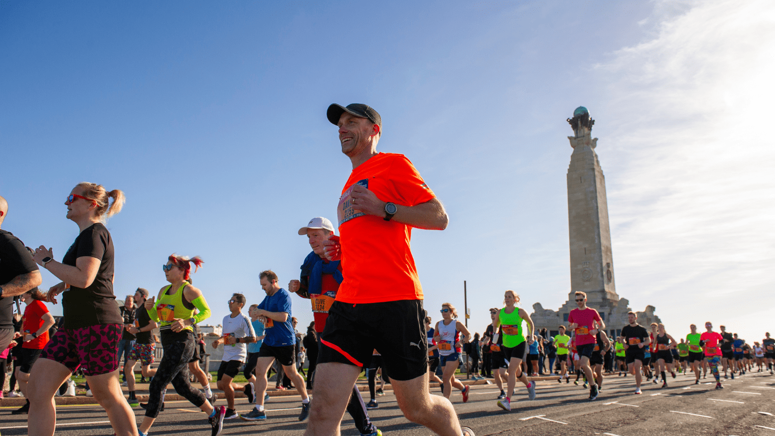Group of runners passing a tall monument under clear blue skies during a marathon.