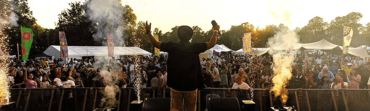 Singer on stage facing a cheering crowd with fireworks and smoke effects at sunset.