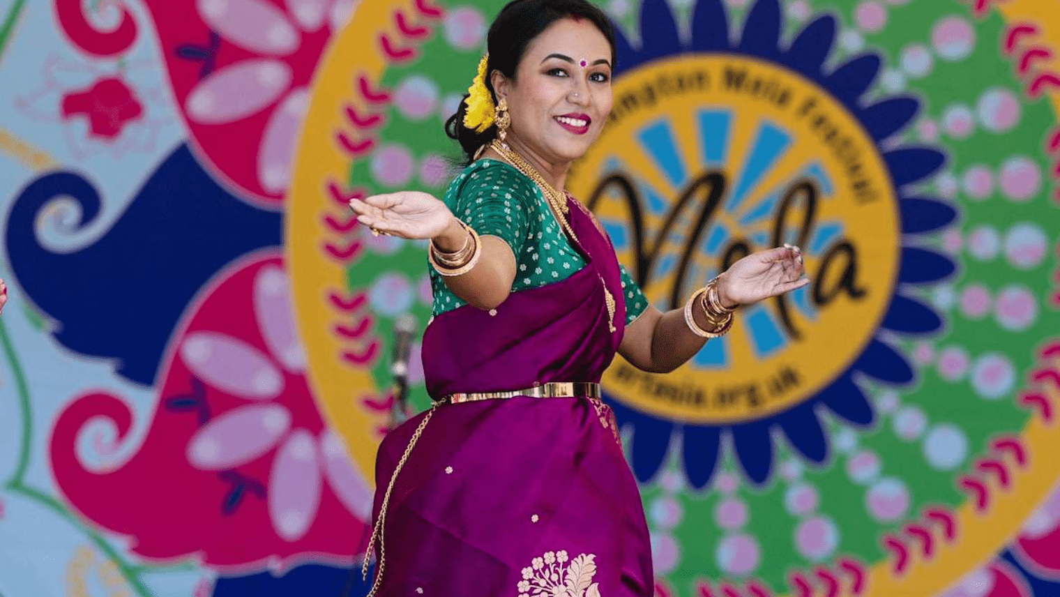 Dancer in vibrant sari performing traditional Indian dance against a colourful “Mela” festival backdrop