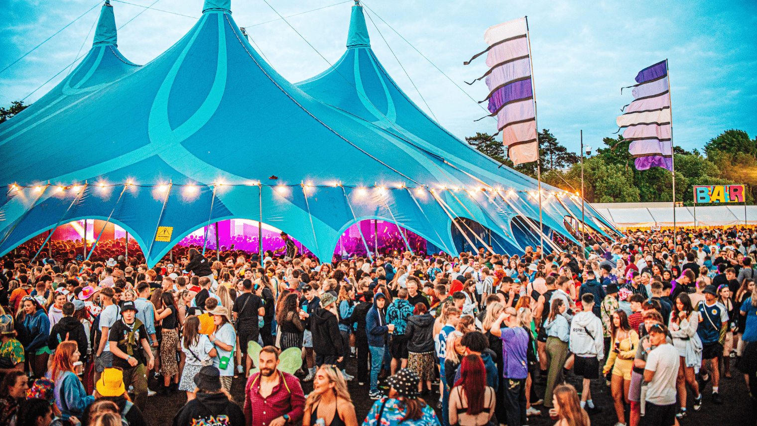Festival tent with crowds of people in and around it 