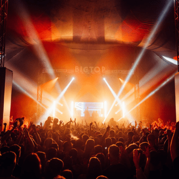 Packed audience inside a tent facing a brightly lit “BIGTOP” concert stage.