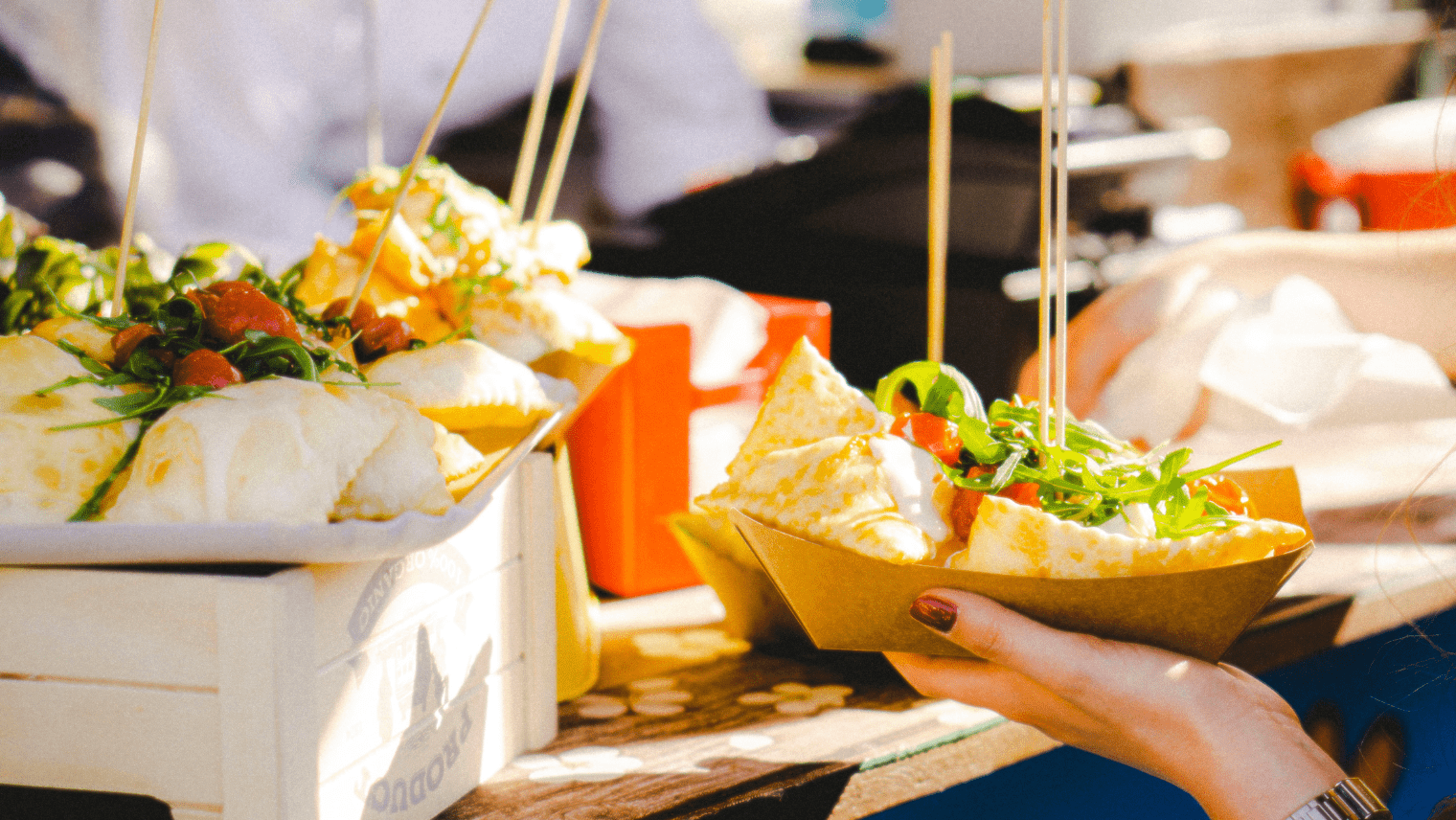 Fresh flatbread wraps filled with greens and tomatoes, served in paper trays at an outdoor market.