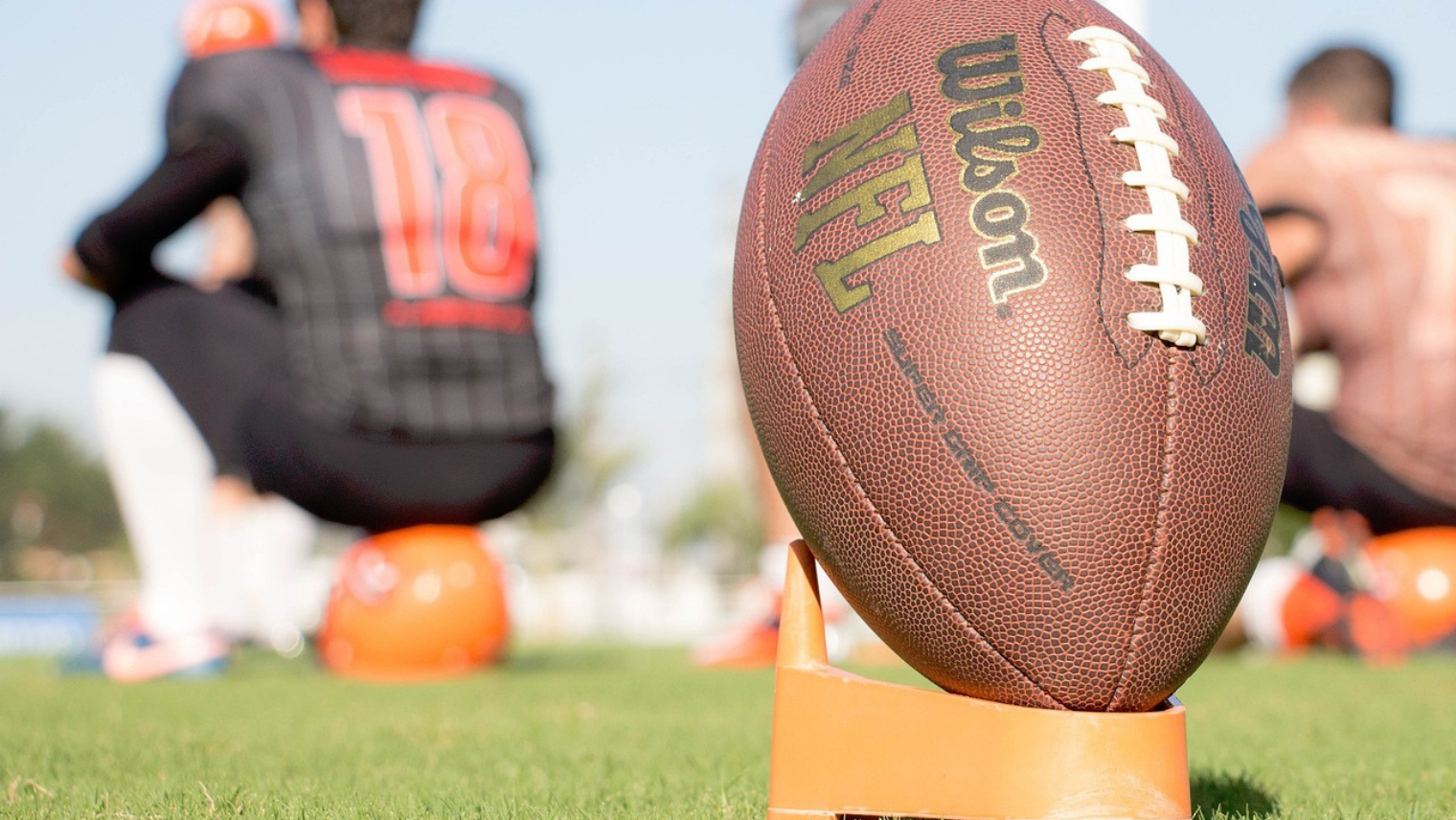 American football on a pitch with player sat in front of it