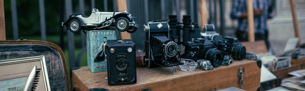 Vintage cameras and small antiques displayed on a wooden table at an outdoor market.