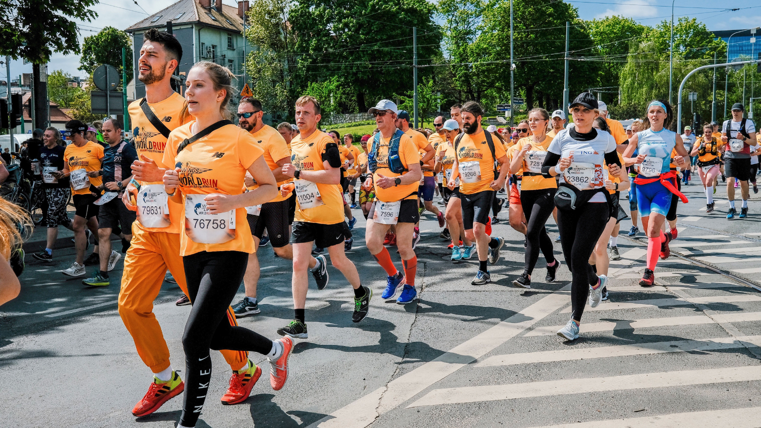  Large group of runners in orange “Wings for Life World Run” shirts participating in a city race under clear skies.