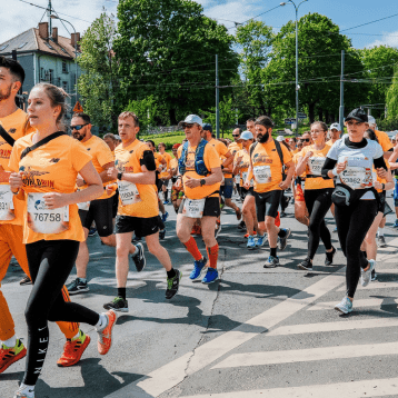  Large group of runners in orange “Wings for Life World Run” shirts participating in a city race under clear skies.