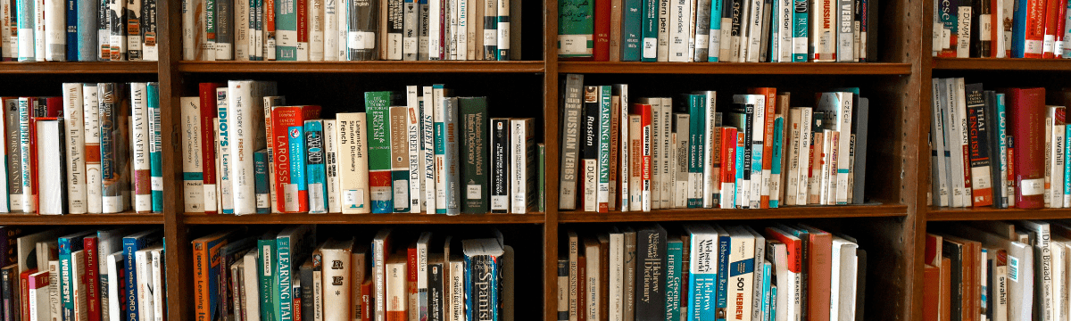 A library bookshelf filled with a variety of books, many focused on language learning and reference. The spines show titles such as French dictionaries, grammar guides, and other educational texts, all neatly arranged with library labels.