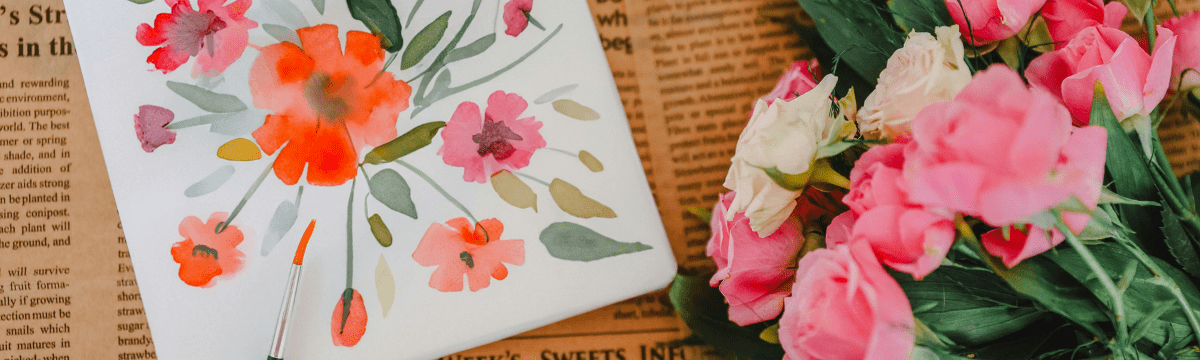 A floral watercolor painting with orange and pink flowers lies beside a bouquet of pink roses on newspaper pages.