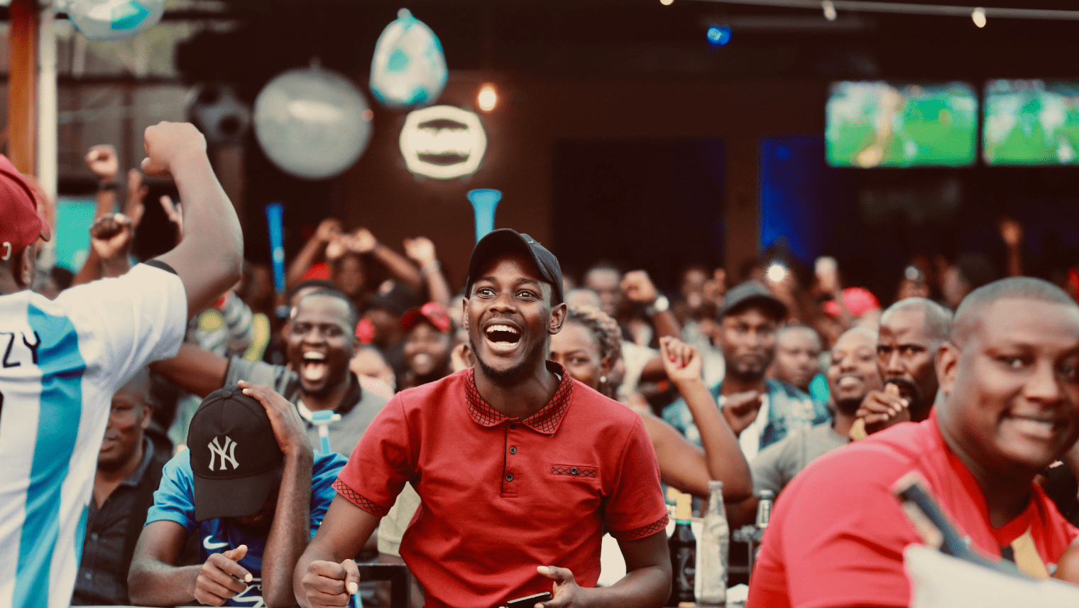 Excited crowd watching a football match indoors, cheering and celebrating together.