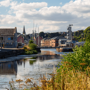 A bright harbor packed with boats, with a Ferris wheel and hillside buildings behind.