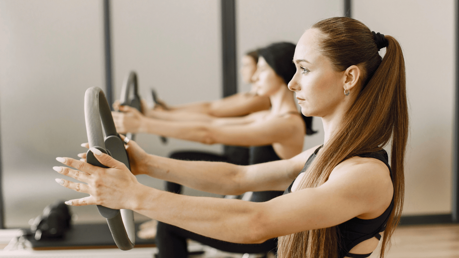 Three women practicing Pilates in a gym, focusing on their poses on exercise mats.