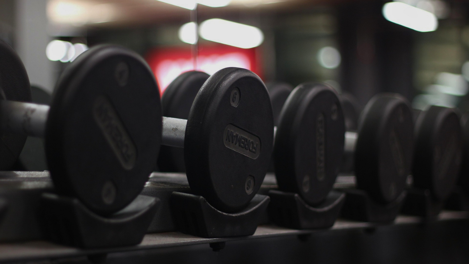 Several black dumbbells neatly lined up on a rack in a dimly lit fitness centre.