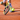  A tennis racket with a yellow and black frame hovers near a bouncing yellow ball on a reddish clay court, with a player’s shoes and white boundary lines visible.