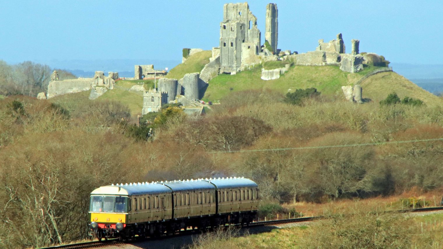 A passenger train running on the Swanage Railway line with Corfe Castle in the background - South Western Railway