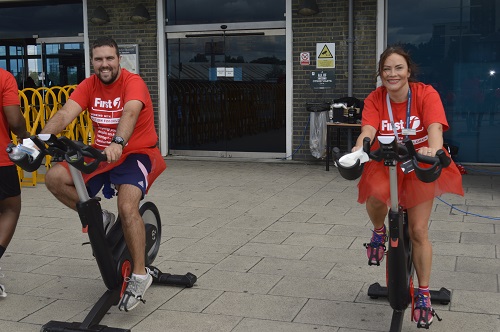 A male and a female SWR staff member on exercise cycles, dressed in red t-shirts and matching tutus