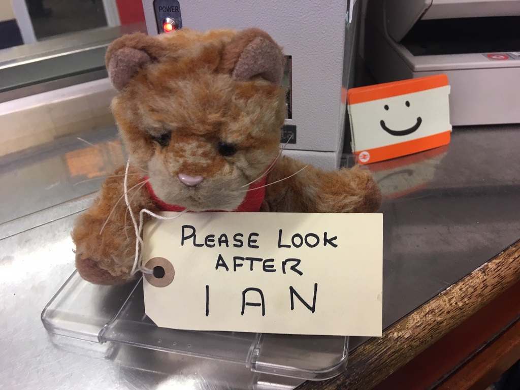 Tom the station cat (a stuffed children's toy on a desk, with a luggage label)