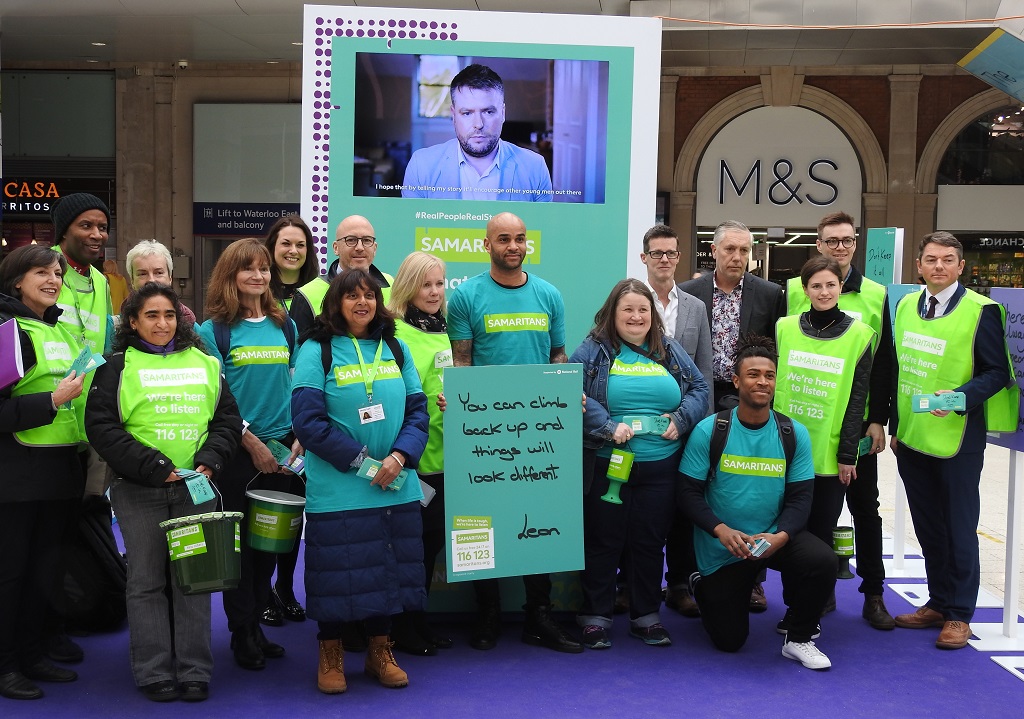 Group of Samaritans Volunteers and SWR staff standing in front of a Samaritans banner