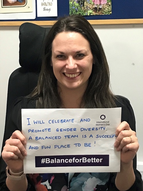 Body Image - Jenny Saunders, Head of Stations and Revenue Protection. Jenny is holding a sign which says 'I will celebrate and promote gender diversity. A balanced team is a successful and fun place to be! #BalanceforBetter'