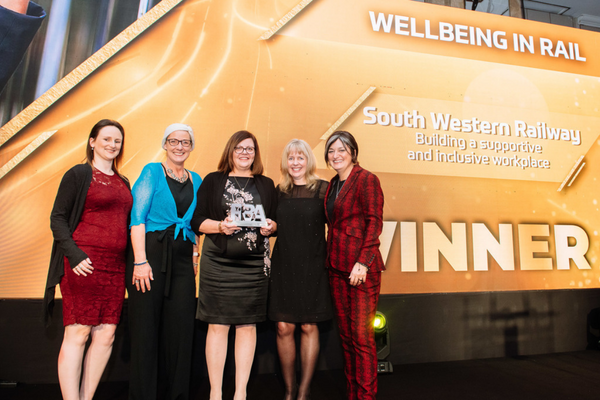 Group of five women standing together with the central one holding an award
