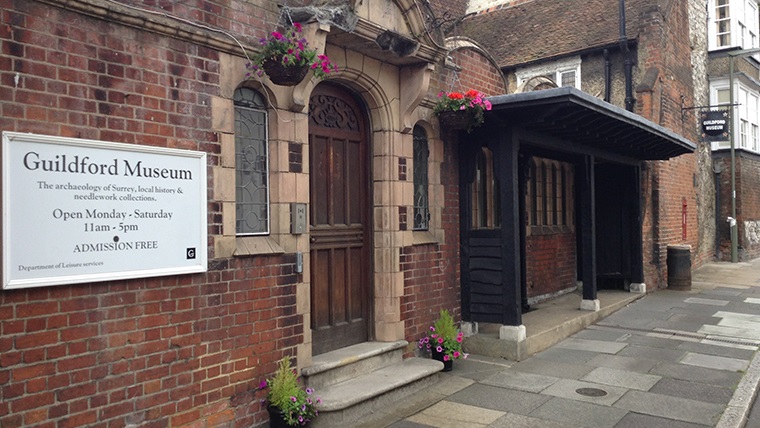 Front entrance to the Guildford Museum. A sign on the wall to left of the door reads: 'Guildford Museum. The archaeology of Surrey, local history and needlework collections. Open Monday - Saturday 11am-5pm. Admission Free.'