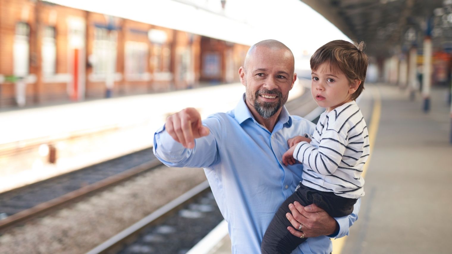 A father pointing out a train to a child being held in his arms
